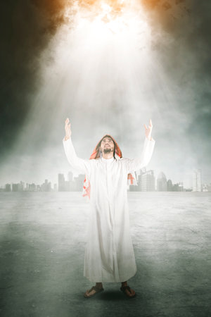 Arabian man raising his hands while praying to the Allah and standing under bright light with modern city backgroundの写真素材