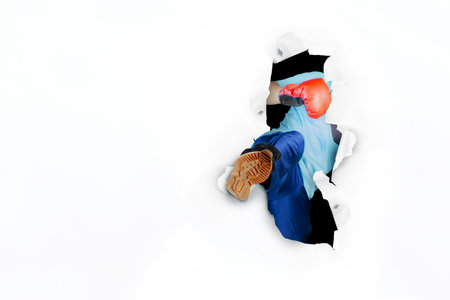 Picture of unknown man wearing boxing gloves while kicking through torn paper with copy space....