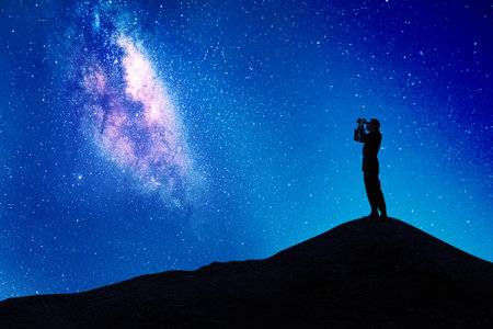 Silhouette of male manager using binoculars to looking at milky way in the night sky while standing on the hill peakの写真素材