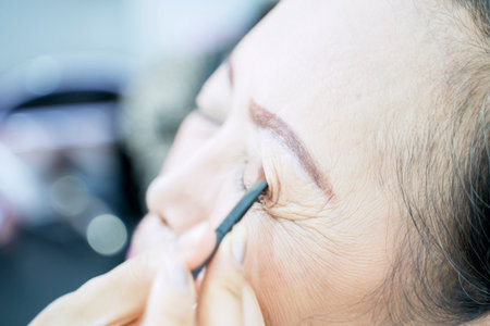 Close up of old woman applied eyeshadow by her makeup artist while preparing to photoshootの写真素材