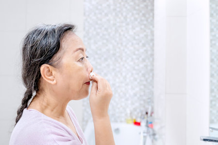 Close up of old woman cleaning her face with cotton pads while doing treatment her face skin in the bathroom . Shot at homeの写真素材