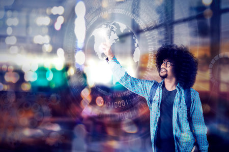 Double exposure of Afro male college student holding a book while pressing a globe on the virtual screen with blurred lights backgroundの写真素材