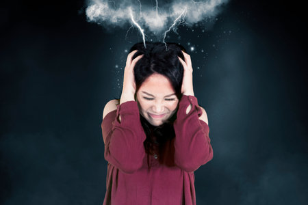 Close up of stressed young woman suffering headache with attacking lightning her head in the dark roomの写真素材