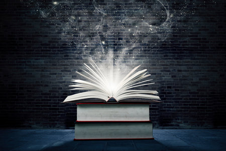 Close up of bright open book with flipped pages on a stack of books with brick wall backgroundの写真素材