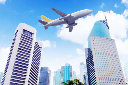 Low angle view of airplane flying low above modern skyscrapers under blue sky