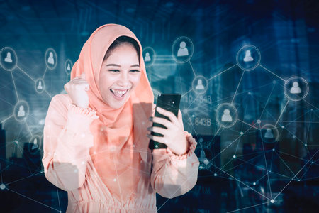 Double exposure of happy Muslim woman using a mobile phone while standing with social media connection network backgroundの写真素材