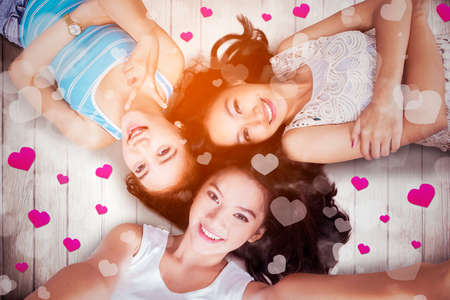 Top view of three teenage girls smiling at the camera and taking selfie while lying together with heart symbolsの写真素材