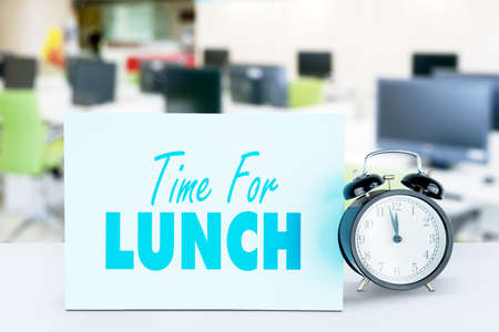 Close up of alarm clock with time for lunch text on empty office room background