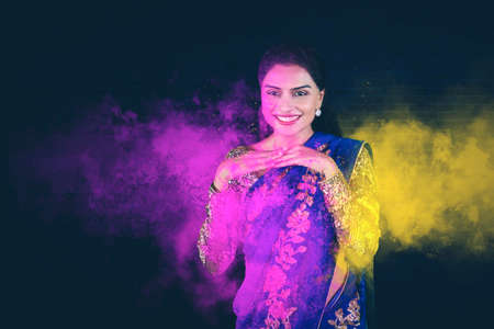 Cheerful young woman with exploding colorful powders at Holi festival of colors in dark backgroundの写真素材