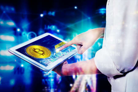 Close up of businesswoman hands using sell and buy bitcoins apps on digital tablet with blurred...