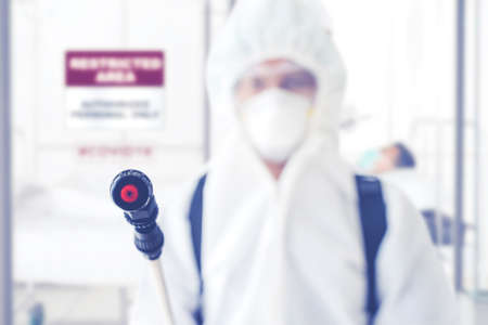 Disinfectant service worker wearing protective suit while cleaning quarantine room with disinfectant...