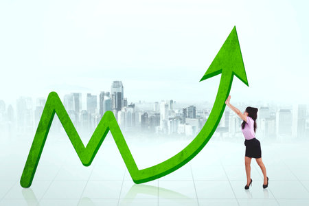 Female entrepreneur pushing an upward arrow while standing with modern city backgroundの写真素材