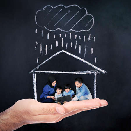 Home insurance concept. Close up of hand holding Muslim family in new house under rain with blackboard backgroundの写真素材