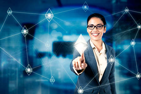 Female manager touching ethereum symbol on virtual screen while standing with blurred sparkling lights background in the officeの写真素材