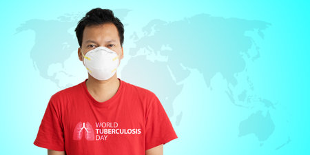 Male volunteer wearing face mask and red clothes with world tuberculosis day text while standing with world map backgroundの写真素材