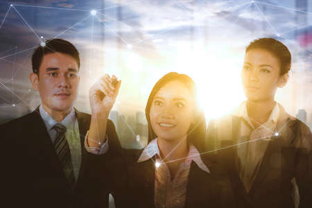 Double exposure of businesswoman drawing connection network while standing with her partners in modern city backgroundの写真素材