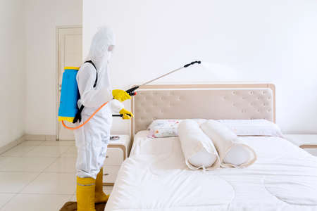 Disinfectant service worker wearing protective suit while spraying bed with disinfectant and removing coronavirus disease in infected patient houseの写真素材
