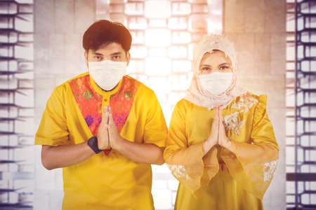 Muslim young couple wearing face mask while showing congratulate hands gesture Eid Mubarak and...