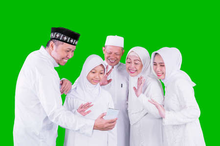 Three generation Muslim family making video call in the studio while celebrating Eid Mubarak. Shot with green screen backgroundの写真素材