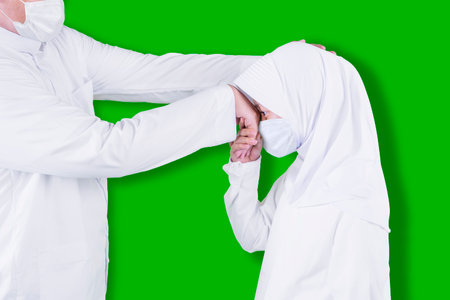 Muslim little girl wearing face mask while handshaking and apologizing to her father during Eid Mubarak in the studio with green screen backgroundの写真素材