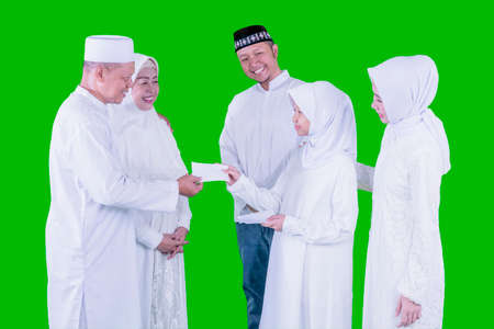 Muslim little girl getting money envelope from her grandparents while standing with her parents...