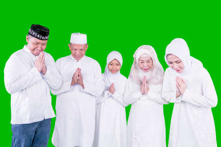 Happy three generation muslim family showing a greeting hands while standing together during Eid Mubarak in the studio with green screen backgroundの写真素材