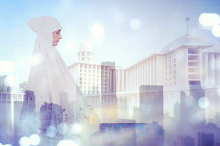 Double exposure of devout Muslim woman doing Salat with mosque and cityscape backgroundの写真素材