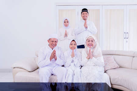 Three generation Muslim family showing congratulate hands gesture Eid Mubarak in the living room. Shot at homeの写真素材