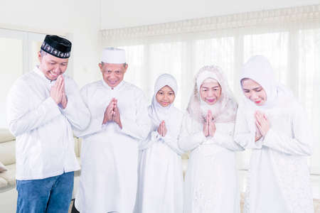 Happy three generation muslim family showing a greeting hands while standing together during Eid Mubarak in the living room at homeの写真素材