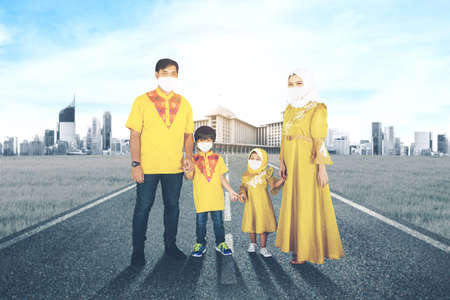 Muslim parents wearing face mask while holding hands their children and standing on the road with mosque backgroundの写真素材