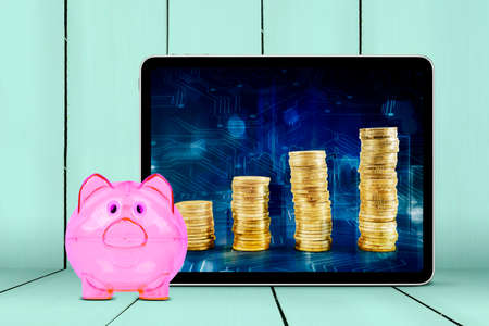 Close up of piggy bank with stack of coin in digital tablet screen with wooden board backgroundの写真素材