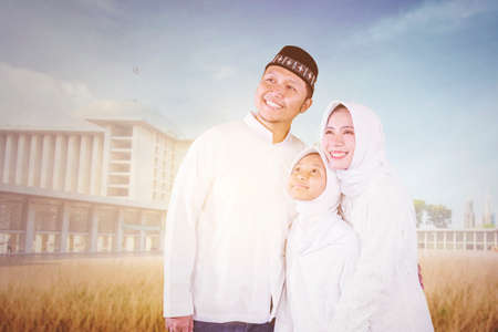 Happy Muslim parents hugging their daughter while standing together in the mosque yardの写真素材