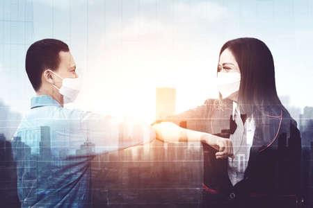Double exposure of two business people wearing face mask while meeting and greeting with elbow in cityscape backgroundの写真素材