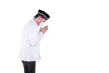 Side view of Muslim man wearing face mask while showing congratulate hands gesture Eid Mubarak and...