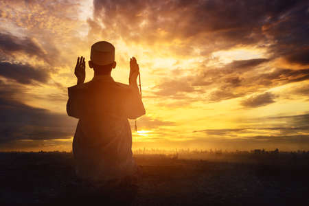 Silhouette of a devout man praying to the Allah while sitting on the hill at sunset time