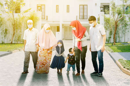 Three generation Muslim family wearing face mask while walking together in the housing with sunlight...