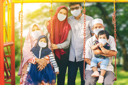 Three generation Muslim family wearing face mask while playing together in the playground during new...