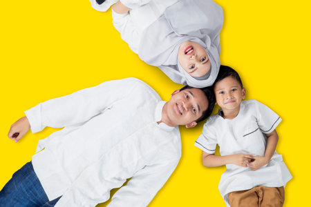 Top view of Muslim parents lying together with their son in the studio with yellow background