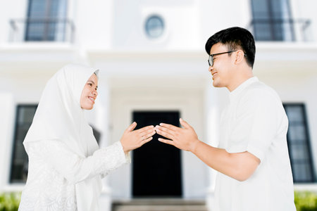 Muslim young woman showing congratulate hands gesture Eid Mubarak to her husband in the front of their houseの写真素材