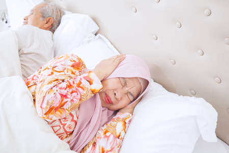 Close up of old Muslim woman annoyed by her snoring husband while sleeping on the bed. Shot at homeの写真素材
