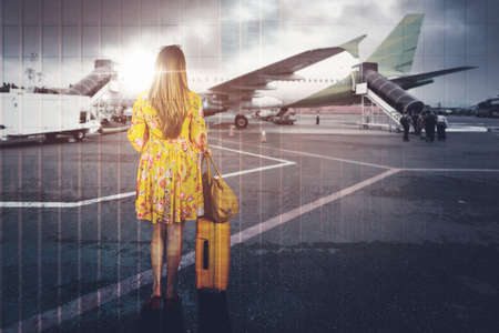 Double exposure of blonde woman carrying luggage and handbag while walking toward airplane with airport backgroundの写真素材