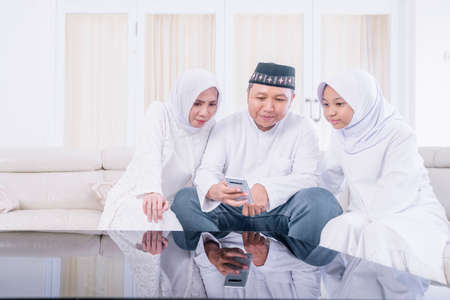 Muslim little girl and her parents making a video call by using a cellphone while sitting together...