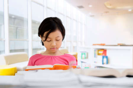 Picture of cute little schoolgirl doing assignment school while reading a book in the library