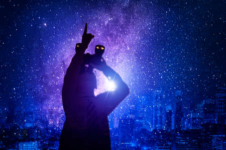 Silhouette of little boy using binoculars while pointing at the night sky and standing with milky way backgroundの写真素材