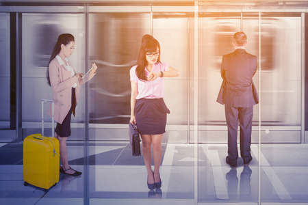 Three business people looks busy while waiting for a train and standing on the platformの写真素材