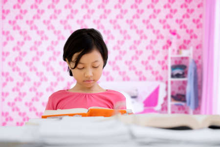 Image of an adorable little girl doing homework while reading a book in the bedroomの写真素材