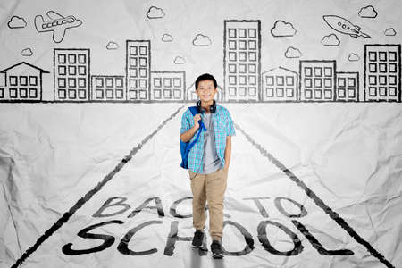 Picture of a handsome preteen student walking above back to school word on the road. Shot with crumpled backgroundの写真素材