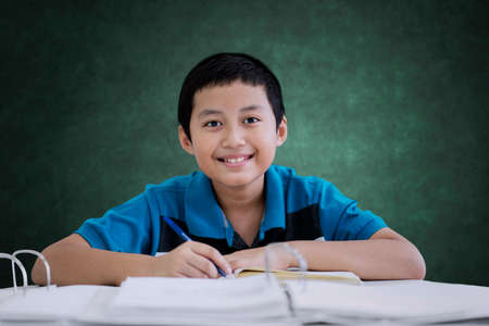 Picture of Asian preteen boy smiling at the camera while taking notes in the classroom