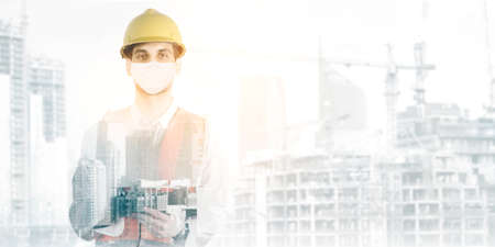 Double exposure of male engineer wearing face mask while standing with construction site building...