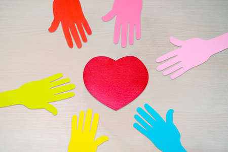 Top view of colorful paper hands with red heart symbol on the wooden tableの写真素材
